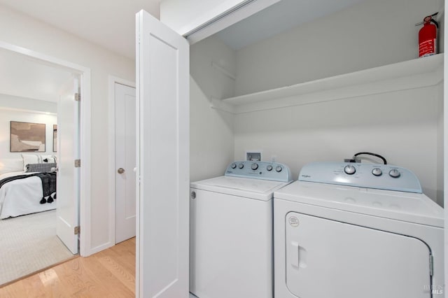 laundry room with washing machine and clothes dryer and light wood-type flooring