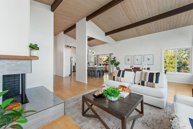 living room with light hardwood / wood-style flooring, an inviting chandelier, lofted ceiling with beams, a tiled fireplace, and wooden ceiling