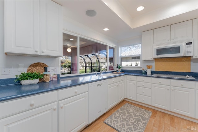 kitchen with white appliances, light wood finished floors, white cabinets, dark countertops, and a sink