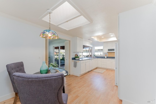 kitchen with dark countertops, light wood-style flooring, ornamental molding, white cabinetry, and pendant lighting