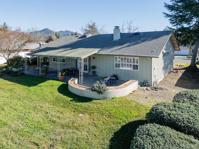 back of house featuring a patio, a chimney, a yard, a mountain view, and board and batten siding