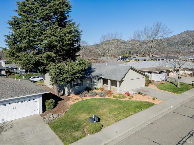 ranch-style home featuring a shingled roof, a mountain view, concrete driveway, and a front yard