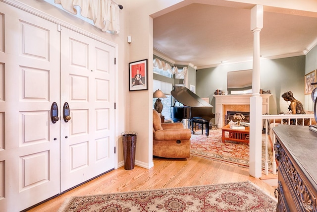 entryway featuring decorative columns, ornamental molding, and light hardwood / wood-style floors