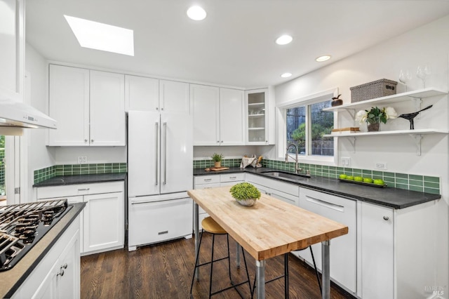 kitchen with sink, white appliances, white cabinetry, a skylight, and dark hardwood / wood-style flooring