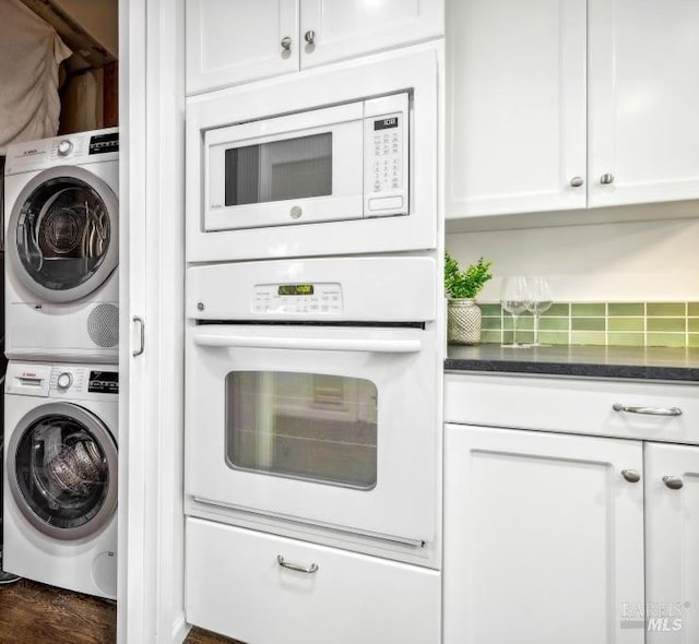 kitchen with stacked washer / drying machine, dark hardwood / wood-style flooring, white appliances, white cabinets, and dark stone counters