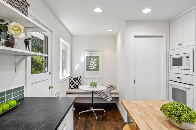 kitchen with backsplash, white appliances, white cabinetry, dark wood-type flooring, and breakfast area