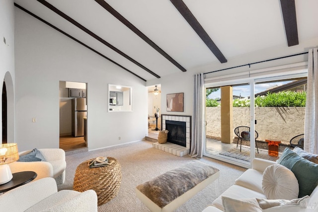 living room with ceiling fan, a tile fireplace, high vaulted ceiling, beamed ceiling, and light carpet