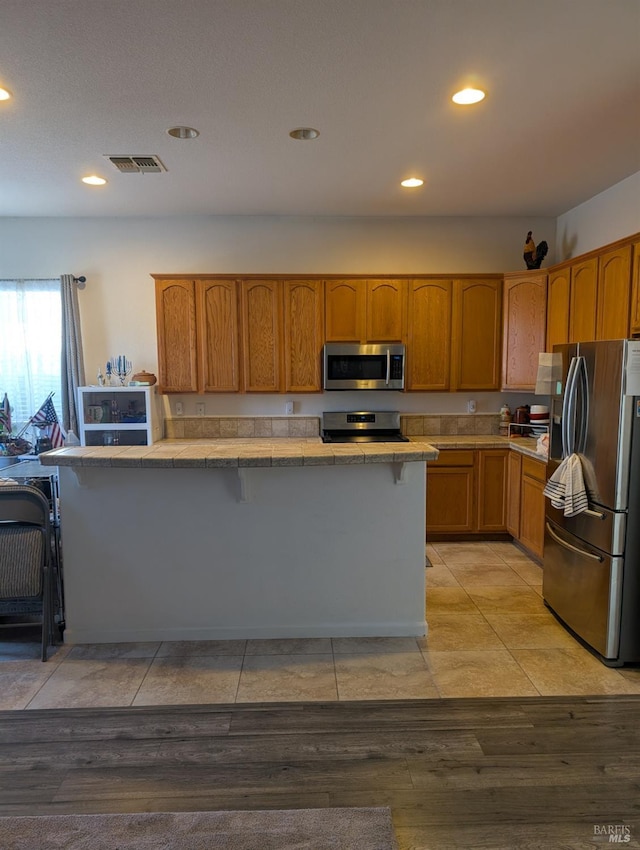 kitchen with appliances with stainless steel finishes, light hardwood / wood-style floors, and a kitchen bar