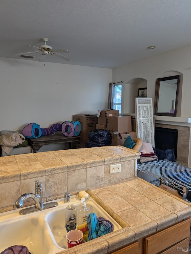 kitchen featuring tile counters, ceiling fan, a fireplace, and sink