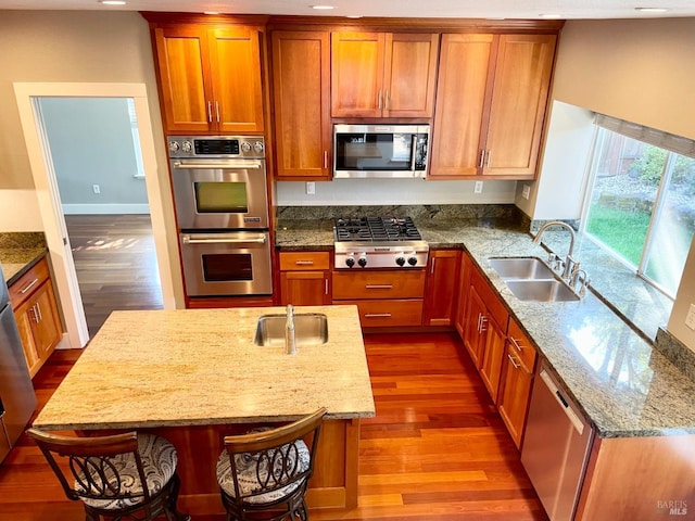 kitchen featuring a breakfast bar, sink, hardwood / wood-style flooring, light stone counters, and stainless steel appliances