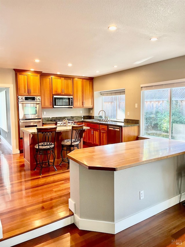 kitchen with a kitchen bar, sink, a textured ceiling, appliances with stainless steel finishes, and hardwood / wood-style flooring