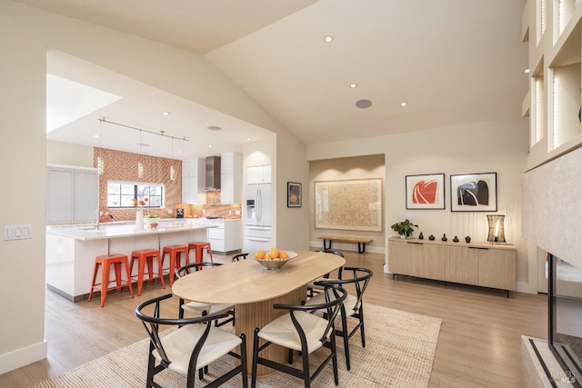 dining space with high vaulted ceiling, light wood-style flooring, and baseboards