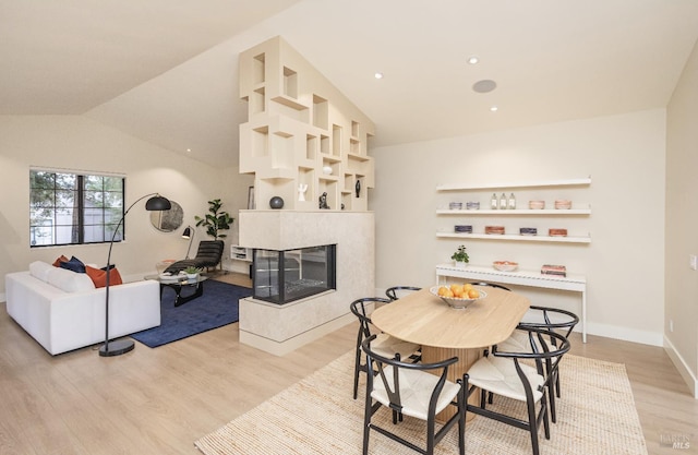 dining area with light wood finished floors, baseboards, vaulted ceiling, a fireplace, and recessed lighting