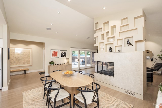 dining room featuring baseboards, light wood-type flooring, high vaulted ceiling, a multi sided fireplace, and recessed lighting