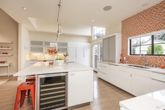 kitchen featuring beverage cooler, light countertops, a kitchen island, and a sink