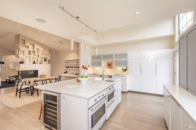 kitchen with decorative light fixtures, a towering ceiling, white cabinetry, light countertops, and a center island with sink