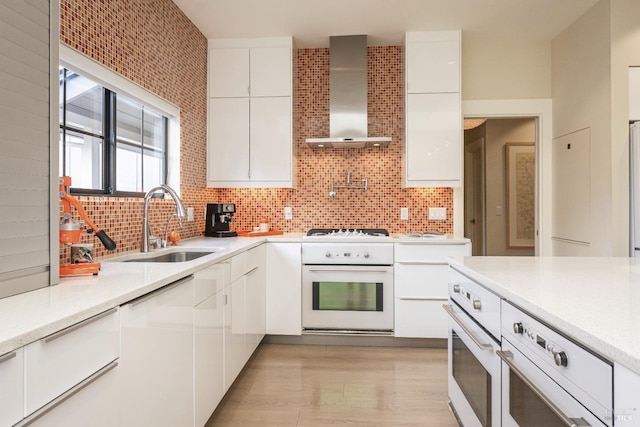 kitchen with white appliances, white cabinets, wall chimney exhaust hood, light countertops, and a sink