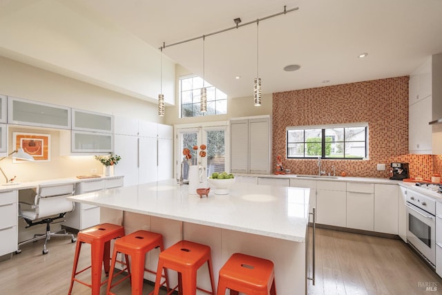 kitchen with stainless steel oven, white cabinetry, a sink, and a center island