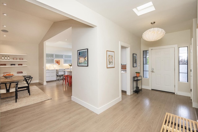 foyer featuring light wood finished floors, a skylight, an inviting chandelier, and baseboards