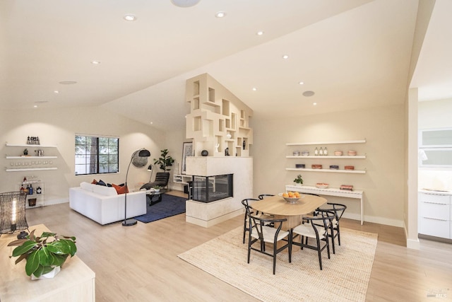 dining space with lofted ceiling, light wood finished floors, a multi sided fireplace, and recessed lighting