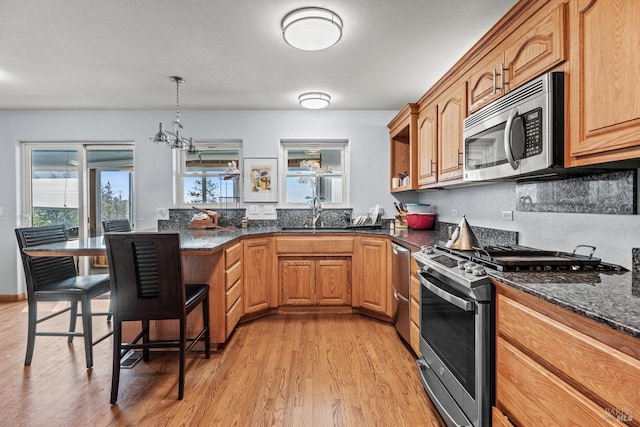 kitchen featuring stainless steel appliances, dark stone counters, sink, hanging light fixtures, and light wood-type flooring