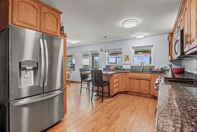 kitchen featuring appliances with stainless steel finishes, decorative light fixtures, sink, light wood-type flooring, and a breakfast bar area