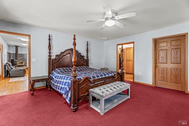 carpeted bedroom featuring ceiling fan and a wood stove