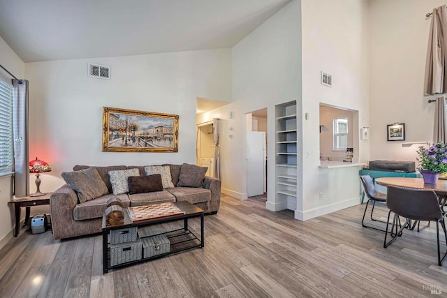 living room with light wood-type flooring, built in features, and high vaulted ceiling