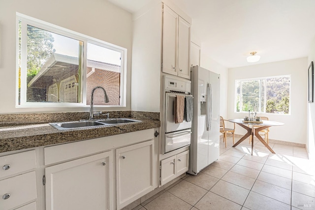 kitchen with light tile patterned floors, white cabinetry, white appliances, dark stone countertops, and sink