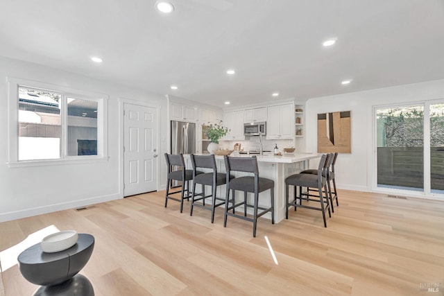 kitchen with white cabinetry, stainless steel appliances, a kitchen island with sink, light wood-type flooring, and a breakfast bar area