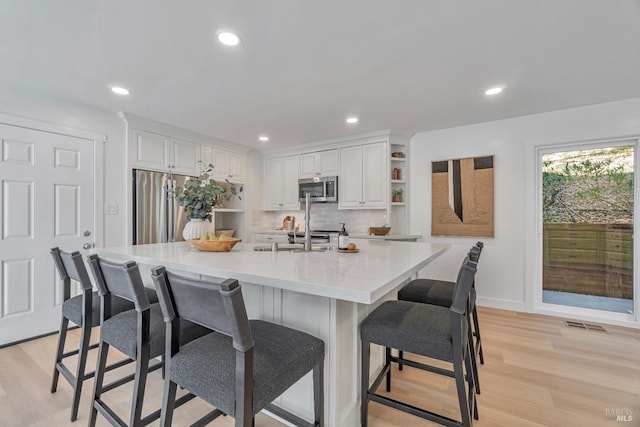 kitchen featuring white cabinets, a kitchen bar, a large island with sink, light hardwood / wood-style floors, and stainless steel appliances