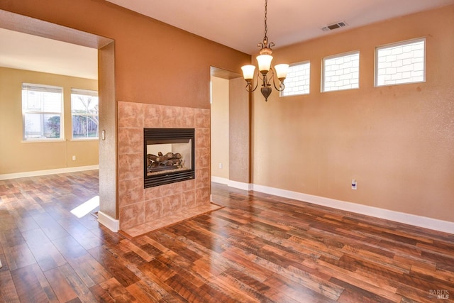 unfurnished living room featuring a tiled fireplace, dark hardwood / wood-style flooring, and a chandelier