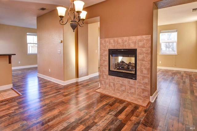 unfurnished living room featuring dark hardwood / wood-style floors, a tile fireplace, and a notable chandelier