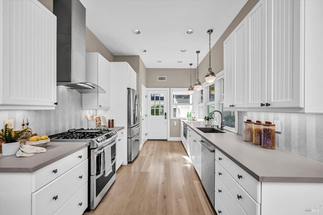 kitchen with stainless steel appliances, hanging light fixtures, wall chimney range hood, white cabinets, and sink