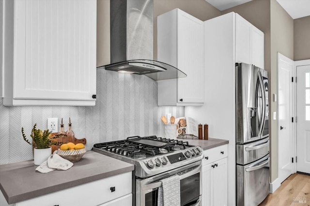 kitchen featuring wall chimney range hood, decorative backsplash, light wood-type flooring, stainless steel appliances, and white cabinets