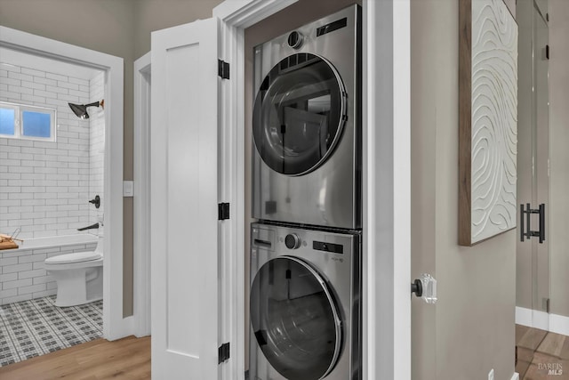 laundry area with stacked washer / drying machine and light wood-type flooring