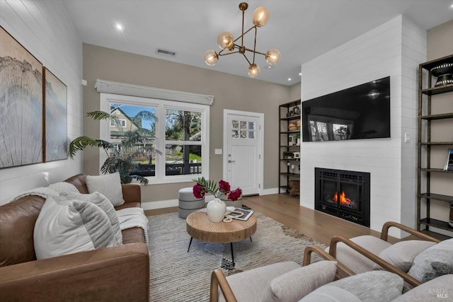 living room with wood-type flooring, an inviting chandelier, and a fireplace