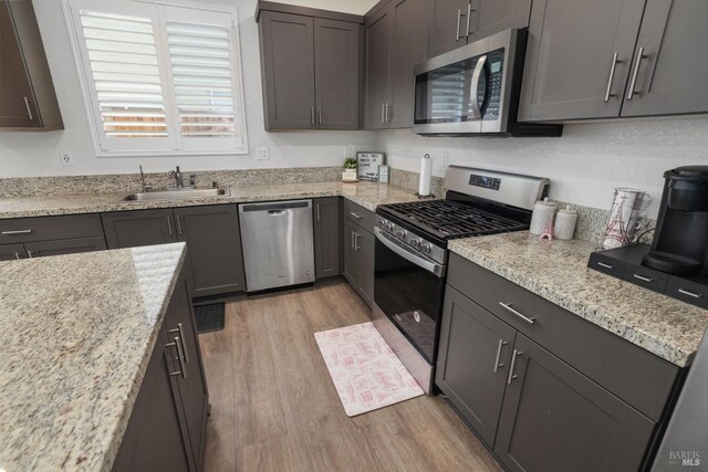 kitchen featuring appliances with stainless steel finishes, sink, light stone counters, and light wood-type flooring