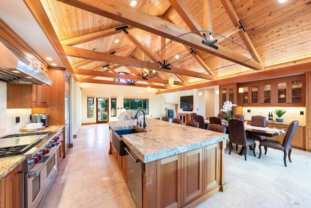 kitchen with ventilation hood, decorative backsplash, stainless steel appliances, a center island with sink, and beam ceiling