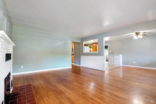 unfurnished living room featuring a brick fireplace, hardwood / wood-style flooring, and ceiling fan