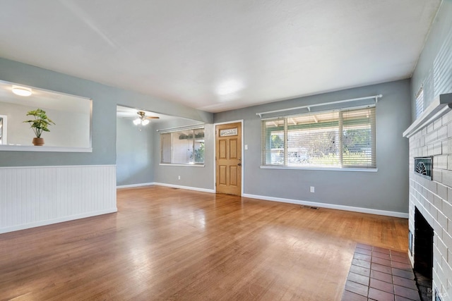 unfurnished living room with ceiling fan, hardwood / wood-style flooring, and a brick fireplace