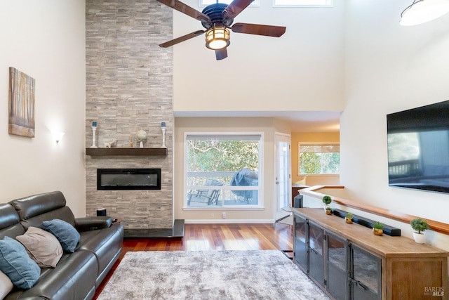 living room with a high ceiling, ceiling fan, hardwood / wood-style flooring, and a fireplace