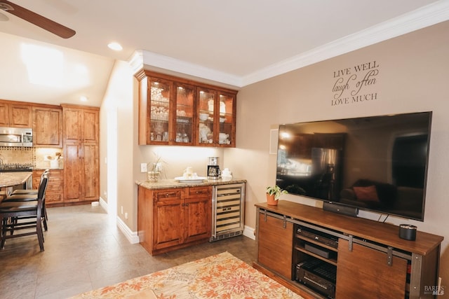 bar with light stone counters, crown molding, beverage cooler, and ceiling fan