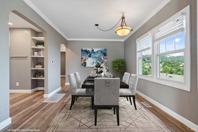 dining space featuring built in shelves, crown molding, and light hardwood / wood-style flooring