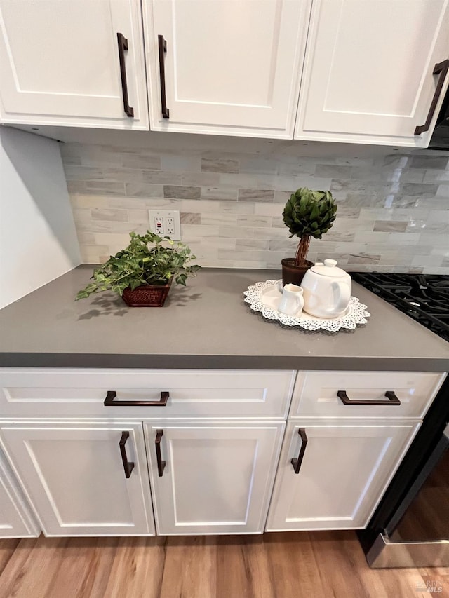 details featuring tasteful backsplash, white cabinetry, stainless steel range with gas stovetop, and light hardwood / wood-style flooring