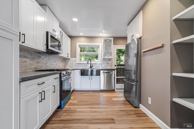 kitchen with sink, backsplash, white cabinets, stainless steel appliances, and light wood-type flooring