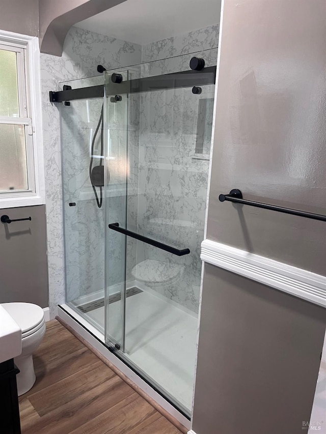 bathroom with wood-type flooring, toilet, and a shower with shower door