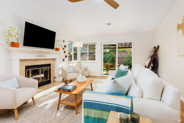 living room featuring ceiling fan, light hardwood / wood-style flooring, and a tiled fireplace