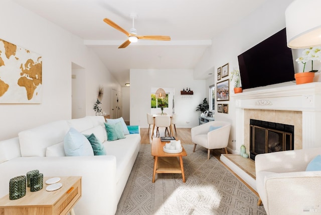 living room with light wood-type flooring, ceiling fan, vaulted ceiling with beams, and a tile fireplace