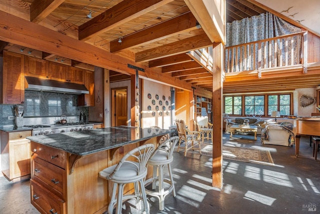 kitchen featuring stainless steel gas stovetop, a kitchen bar, a center island, decorative backsplash, and beamed ceiling